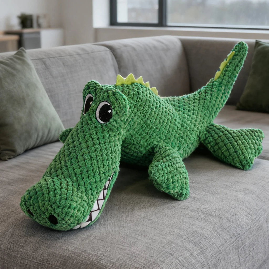 Green crocodile no stuffing squeaky dog toy resting on a gray sofa, showing its textured plush body