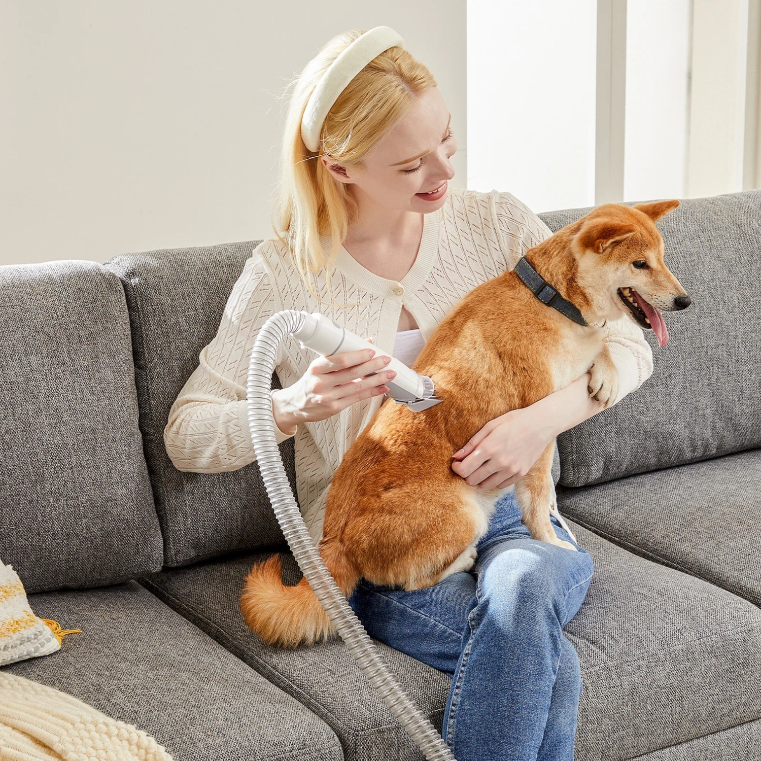 Woman on a couch using a pet grooming vacuum with clippers to trim a calm Shiba Inu held in her lap