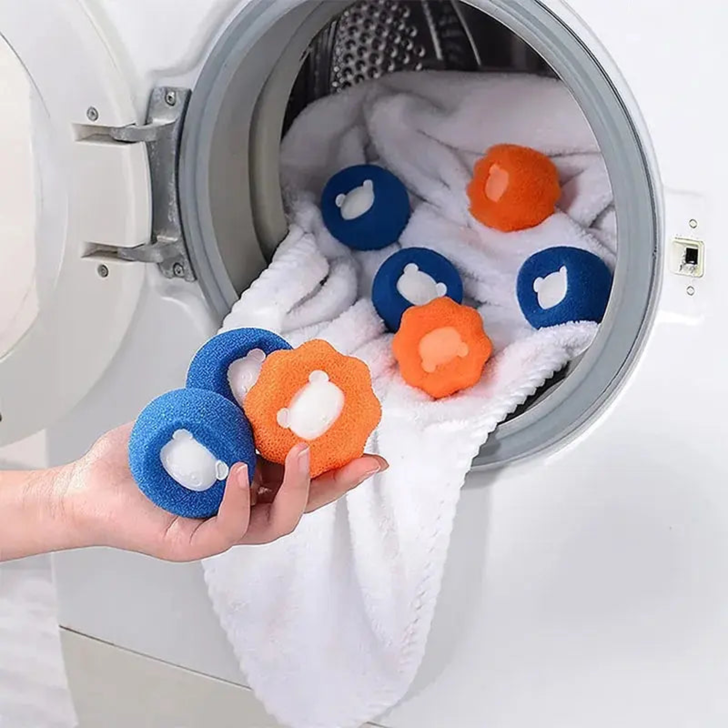 Hand holding blue and orange pet hair remover laundry catchers next to a loaded washing machine